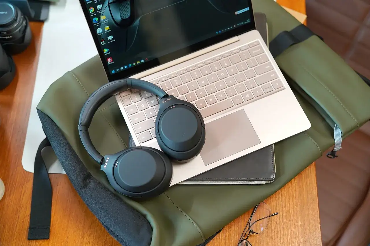 Słuchawki bezprzewodowe Sony leżą na laptopie i zielonej torbie.