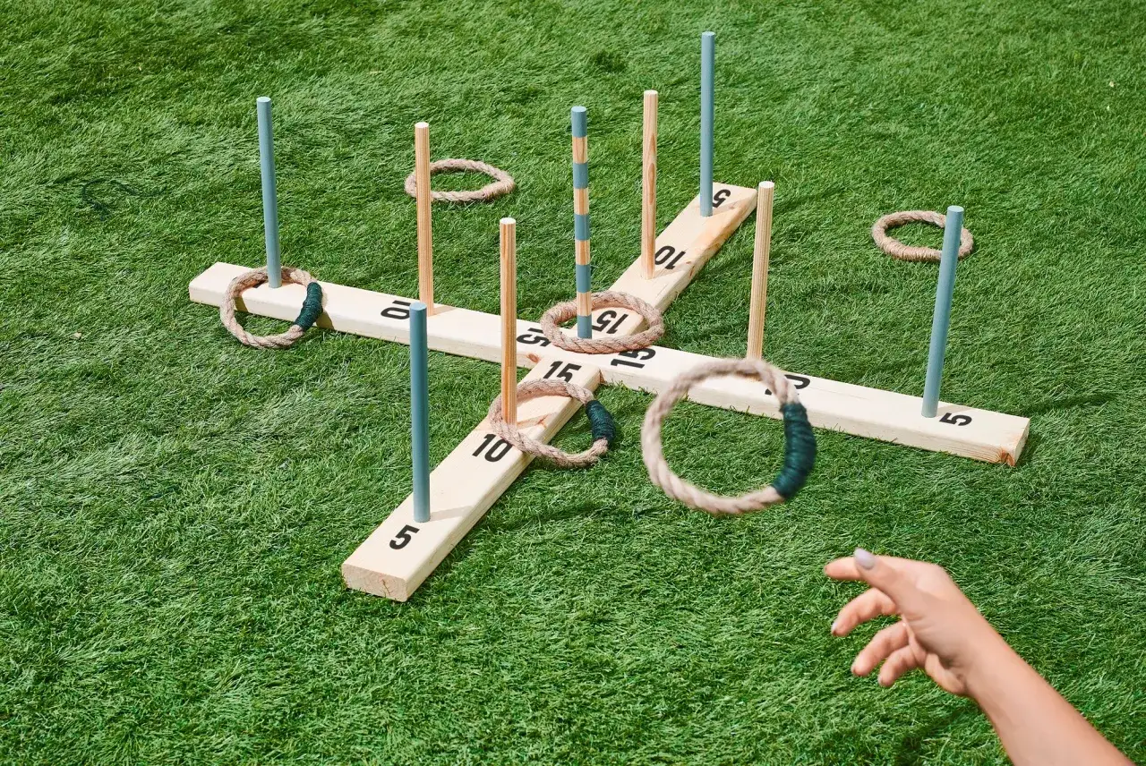 Gra w rzutki na trawie. Ręka rzuca sznurkowy krzyżyk na paliki.