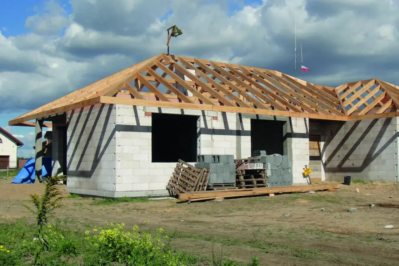 Budowa domku ogrodowego: widoczna konstrukcja dachu z belek drewnianych, ściany z bloczków.