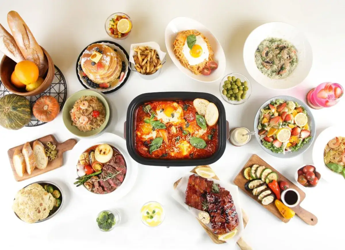 Stół zastawiony różnorodnymi potrawami: mięsa, sałatki, makarony, owoce, pieczywo i desery.