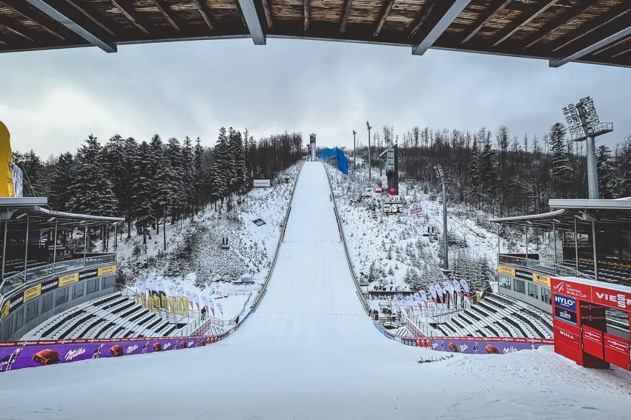 Śnieżna skocznia narciarska w Wiśle, gotowa na puchar świata. Puste trybuny i las w tle tworzą zimowy krajobraz.