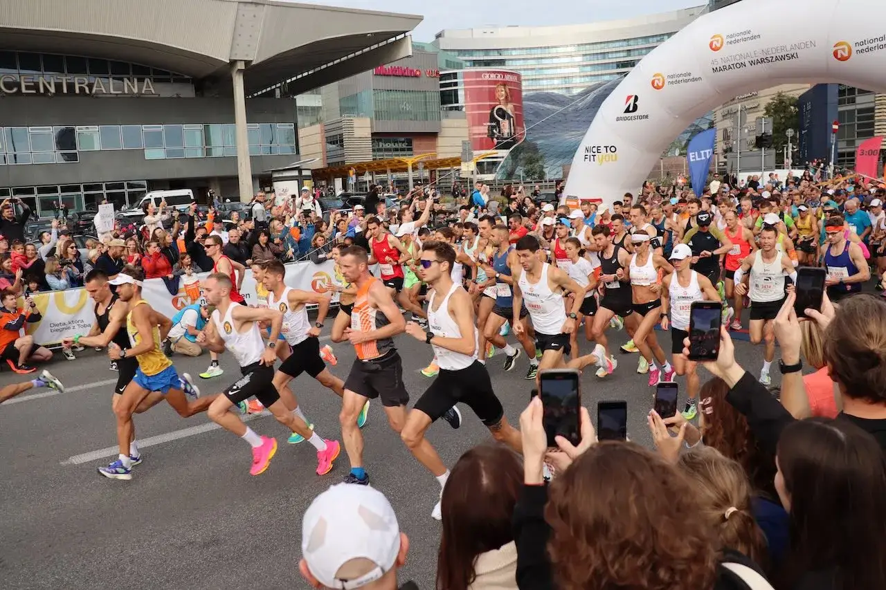 Uczestnicy maratonu w Warszawie, gotowi do startu. To świetny przykład, jak przygotować się do maratonu: trening, determinacja i wsparcie kibiców.