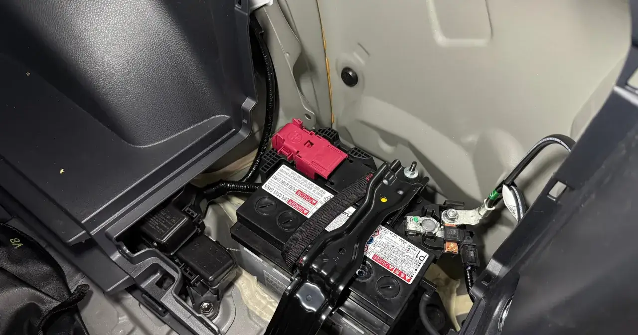 Akumulator 12V w Toyocie Prius znajduje się w bagażniku, pod plastikową osłoną. Widoczne są dwa akumulatory, jeden z czerwonym zabezpieczeniem.