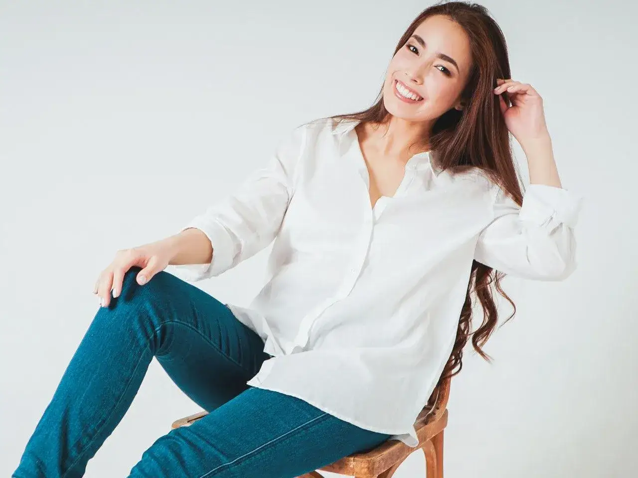 Uśmiechnięta kobieta w białej, długiej koszuli damskiej i jeansach. Stylowa inspiracja, jak nosić długą koszulę damską.
