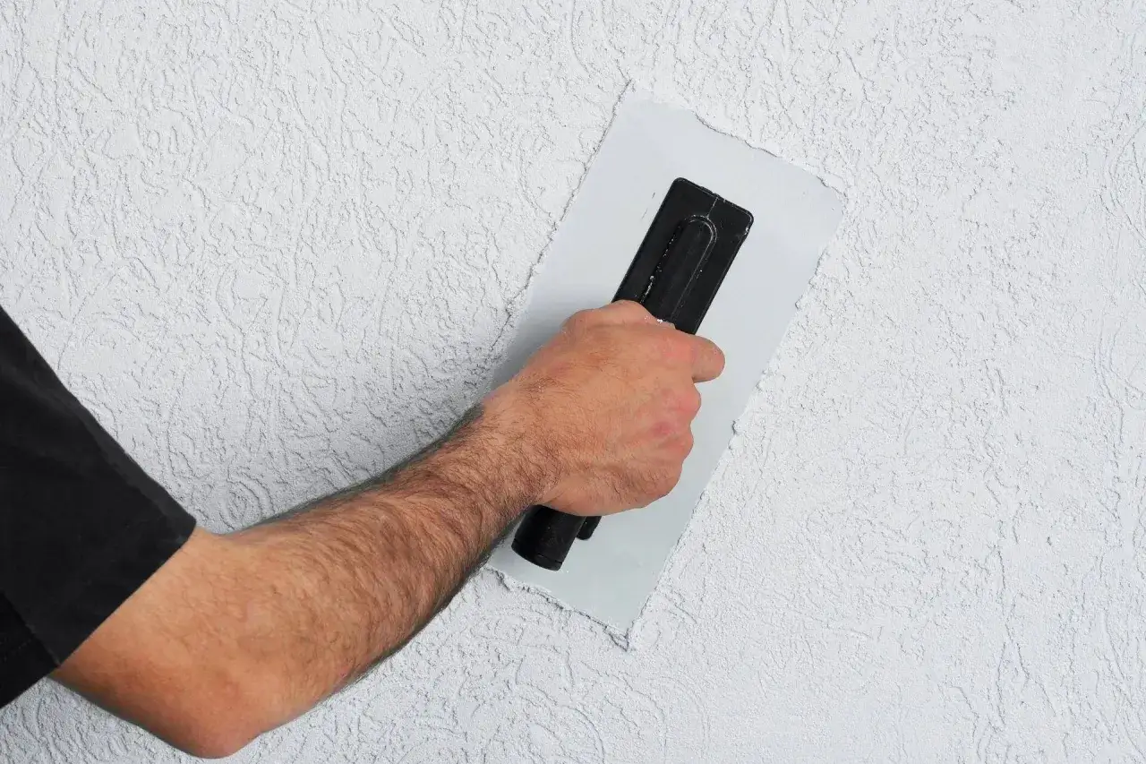 Ręka z kielnią wygładza tynk na styrodurze. Dowiedz się, jak wykończyć styrodur, by uzyskać gładką ścianę.