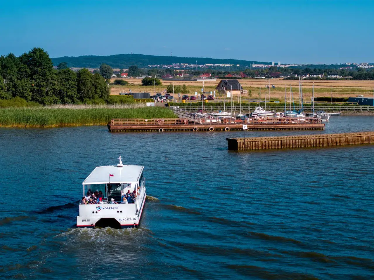 Rejs statkiem "Julek" po wodach, które mogą sugerować, że Koszalin leży nad morzem, z widokiem na przystań jachtową i miasto w tle.