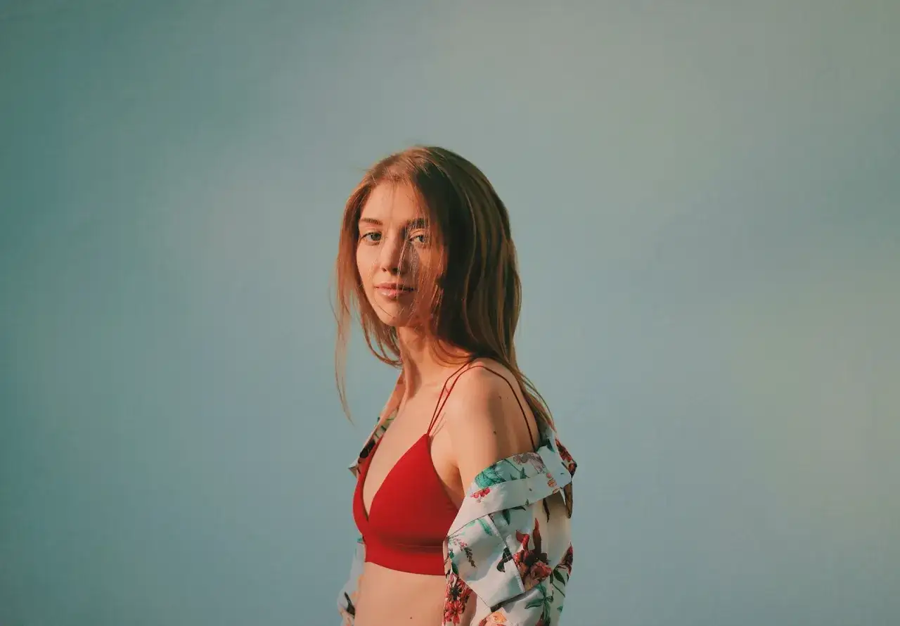 Młoda kobieta w czerwonym staniku i kwiecistej koszuli na jasnoniebieskim tle.