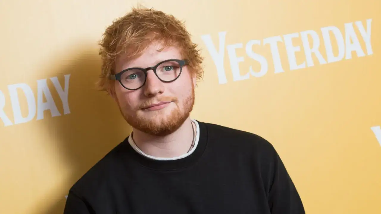 Ed Sheeran w okularach i czarnej bluzie, na tle napisu "YESTERDAY". Wygląda jakby zastanawiał się, kiedy urodził się Ed Sheeran.