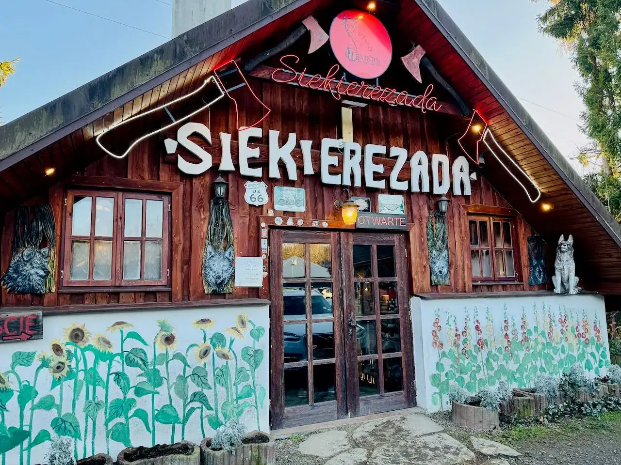 Karczma "Siekierezada" w Polańczyku, Bieszczady. Drewniana chata z neonem, rzeźbami wilków i malowidłami słoneczników.