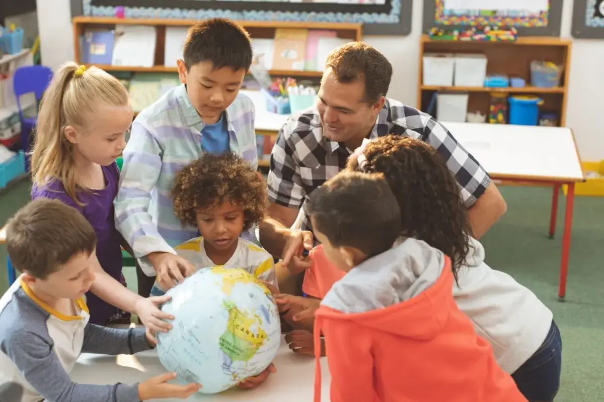 Lehrer und Kinder betrachten gemeinsam einen Globus in einem Klassenzimmer.