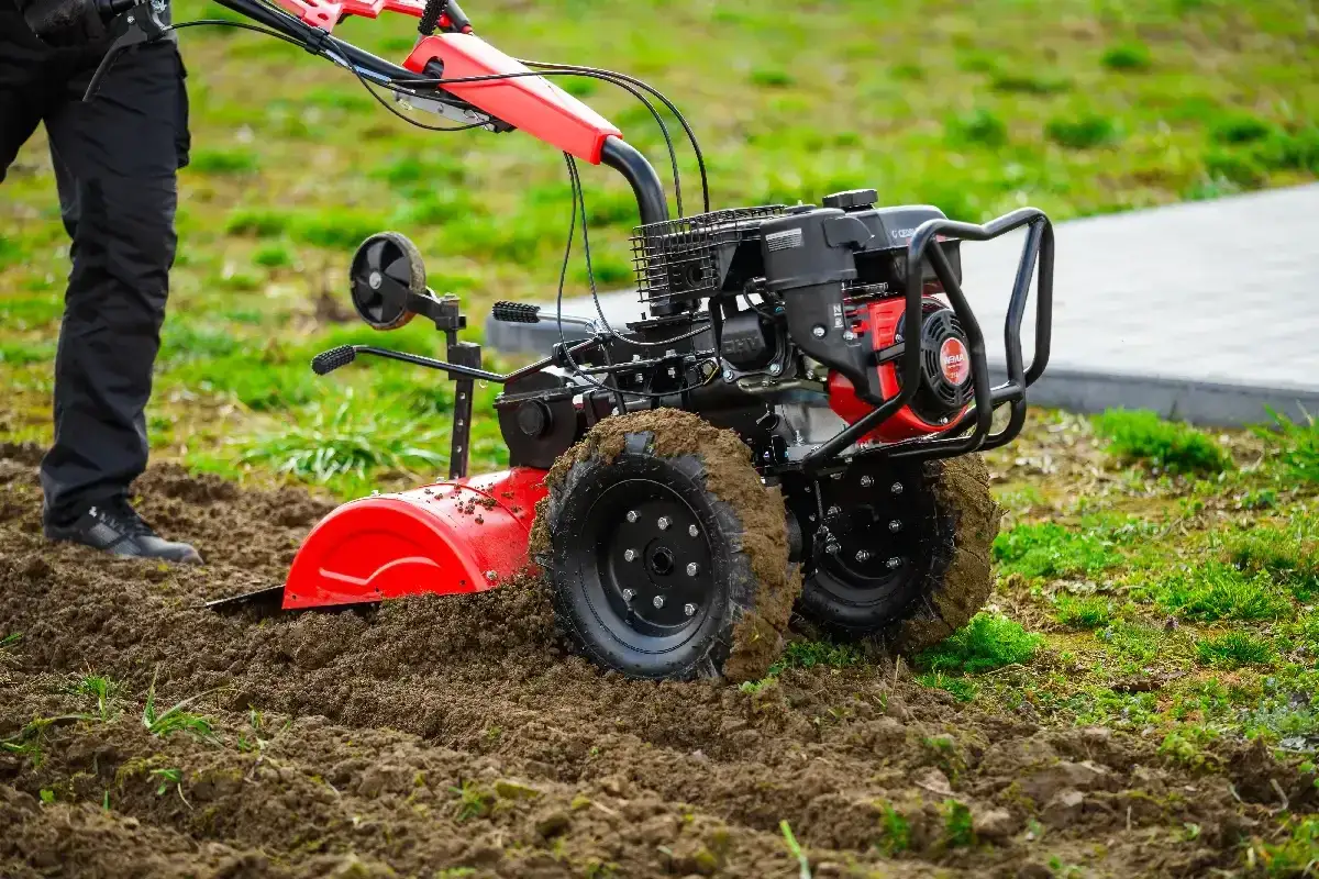 Czerwona glebogryzarka z czarnymi kołami, pracująca na wilgotnej ziemi. Widać jej silnik i uchwyt.