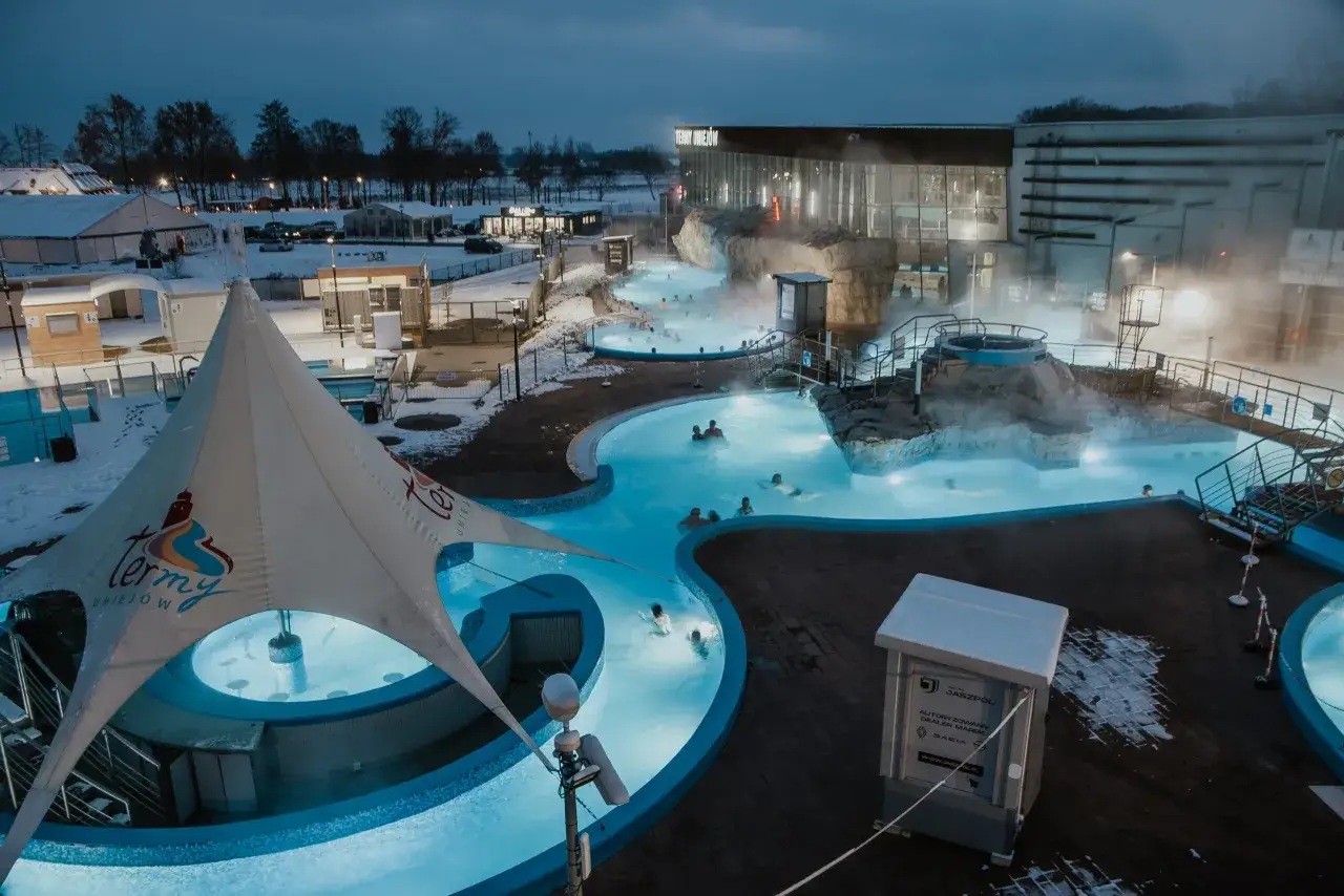 Gdzie są Termy Uniejów? W zimowy wieczór ludzie relaksują się w podgrzewanych basenach zewnętrznych kompleksu.