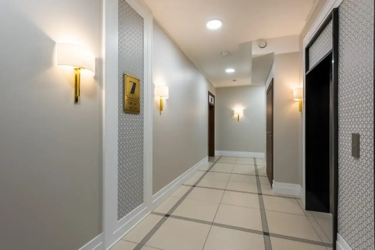 Elegancki korytarz z oświetleniem ściennym i numerem 7. Widać windę i drzwi. Czy ten pasek pod sufitem jest potrzebny?