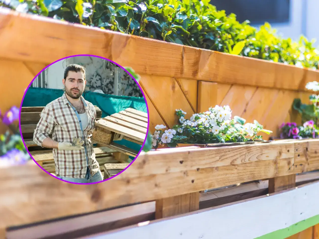 Mężczyzna w kratę trzymający europaletę na tle drewnianego kwietnika z kwiatami.