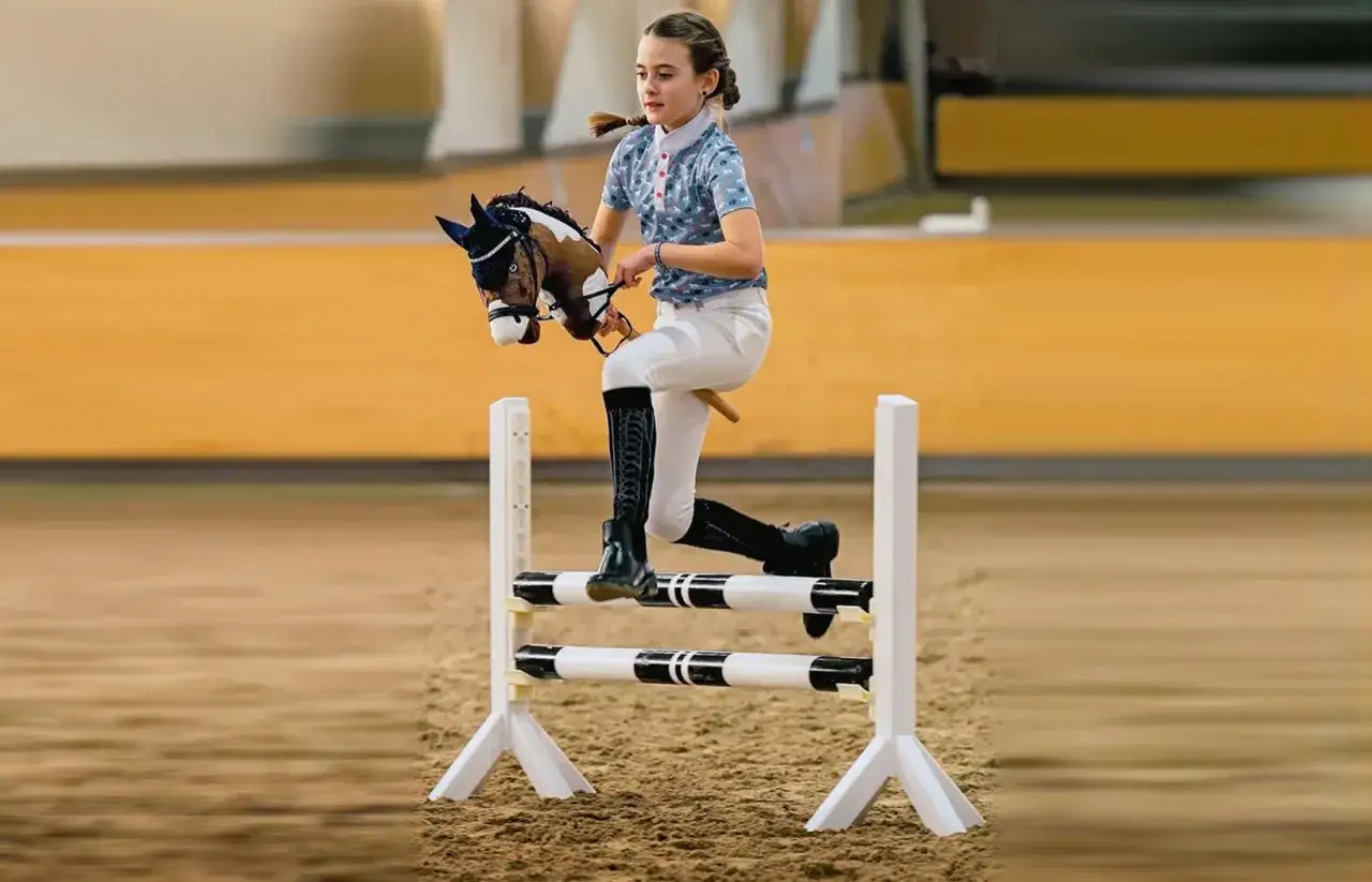 Dziewczynka na kiju, udająca konia, skacze przez przeszkodę. To właśnie jest hobby horse – zabawa w jeździectwo.