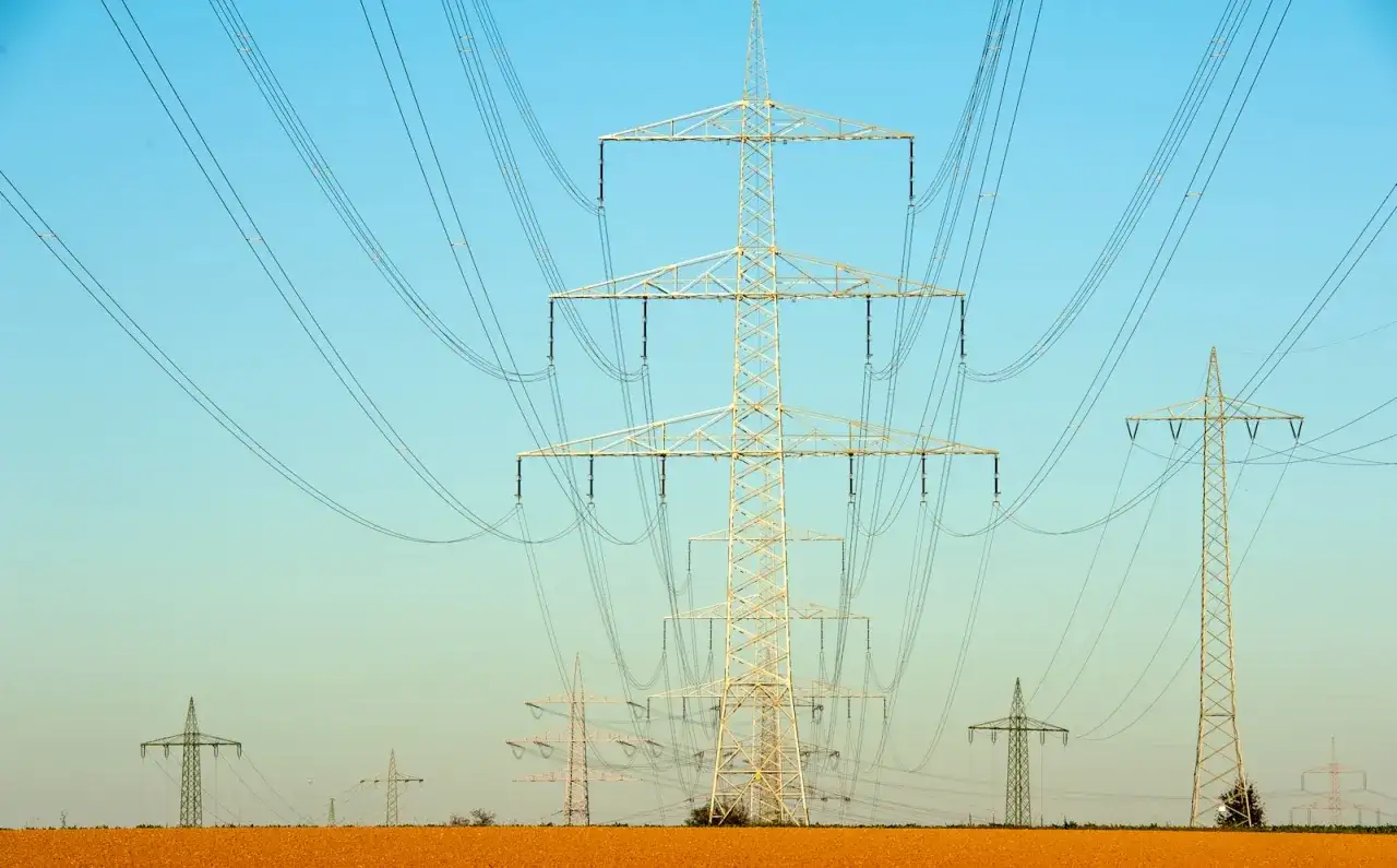 Linie energetyczne przecinają błękitne niebo. Czy ta sieć przesyłowa 1MW ile to kw zasila okoliczne pola?