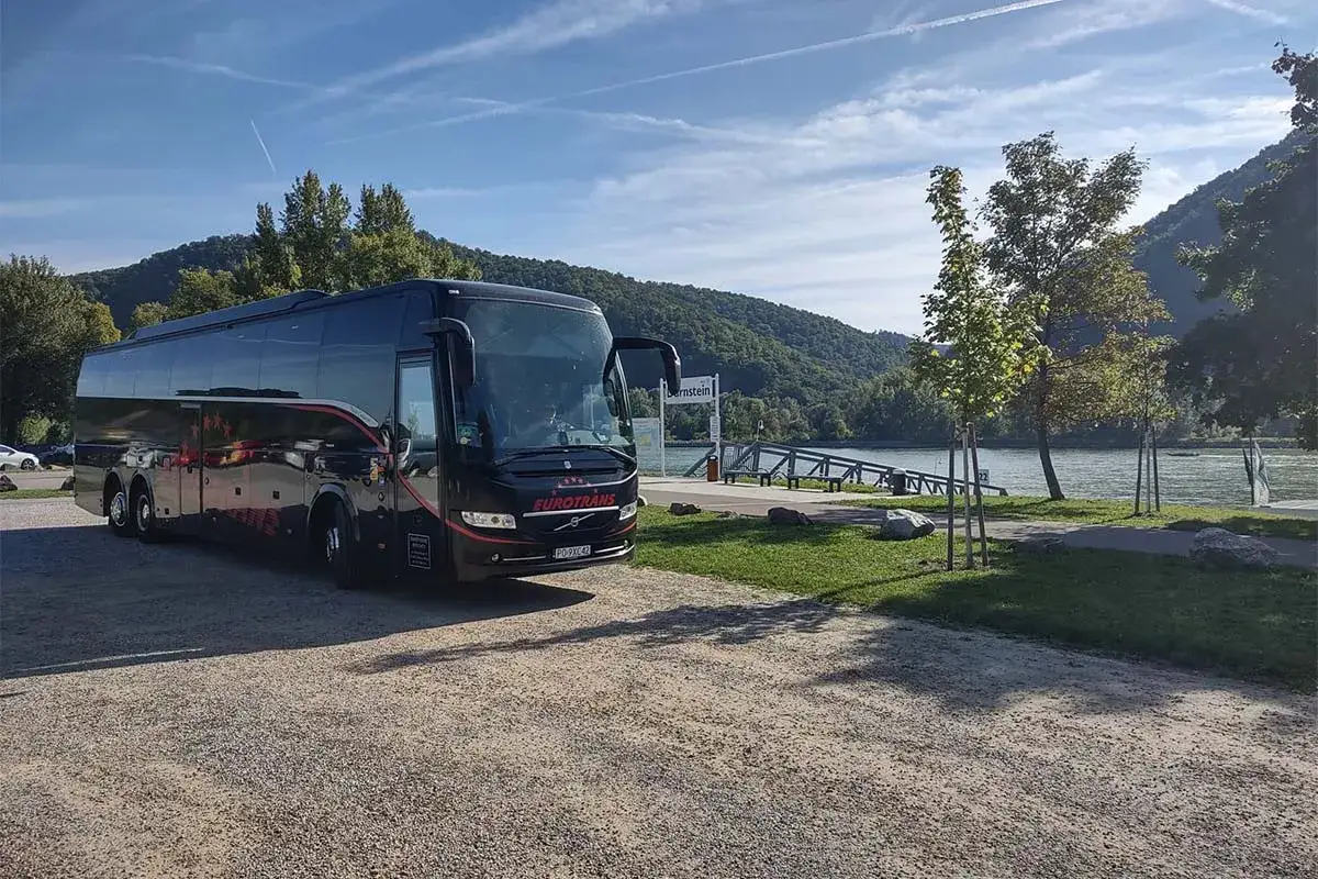 Czarny autokar Eurotrans czeka nad rzeką. Zastanawiasz się, ile się jedzie autokarem do Grecji?