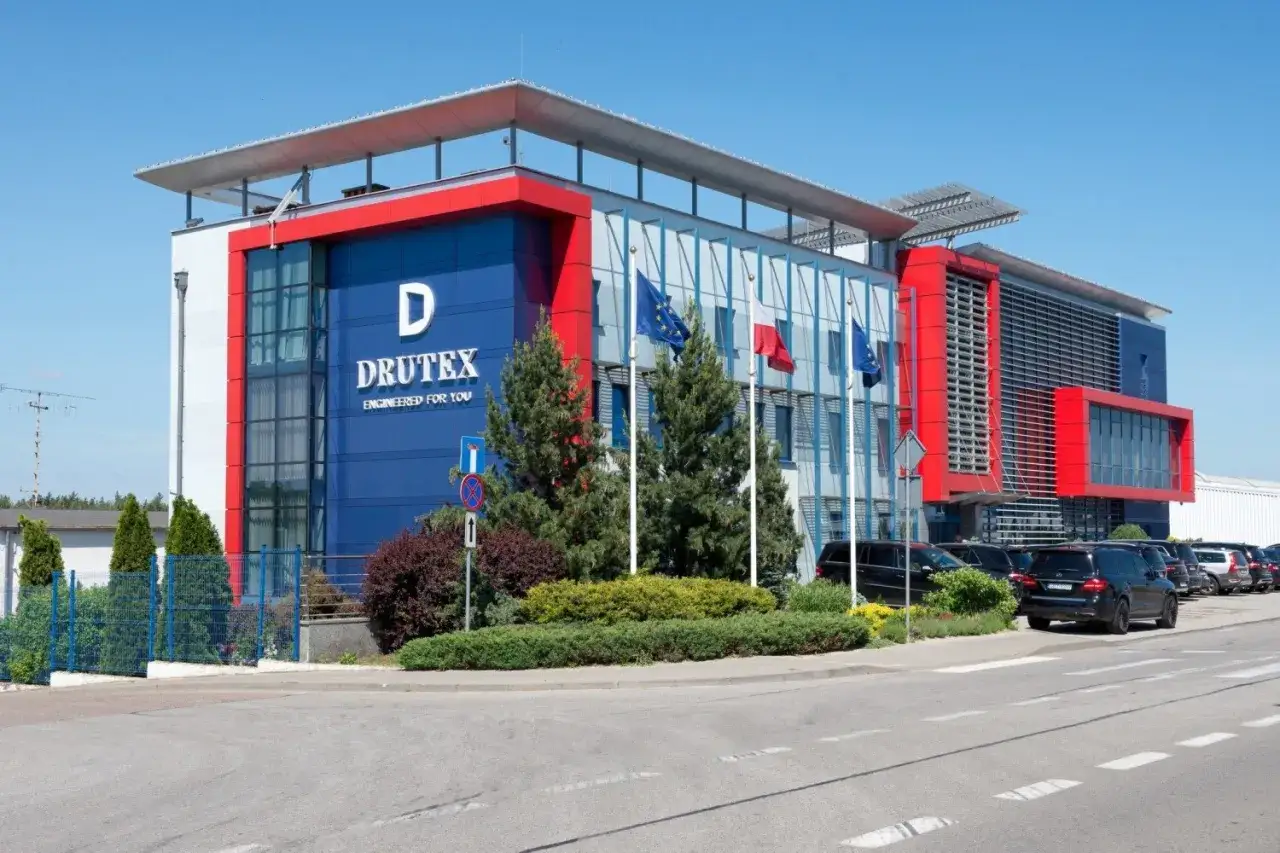 Nowoczesny budynek firmy Drutex w Bytowie z flagami i zielenią.