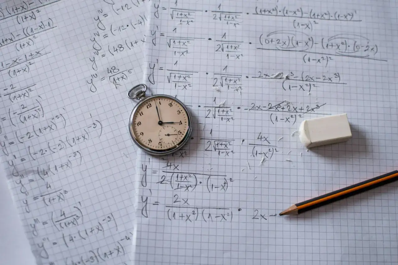 Zegar kieszonkowy obok zeszytu z zadaniami z matematyki. Ile trwa rozszerzenie z biologii? Czas ucieka!