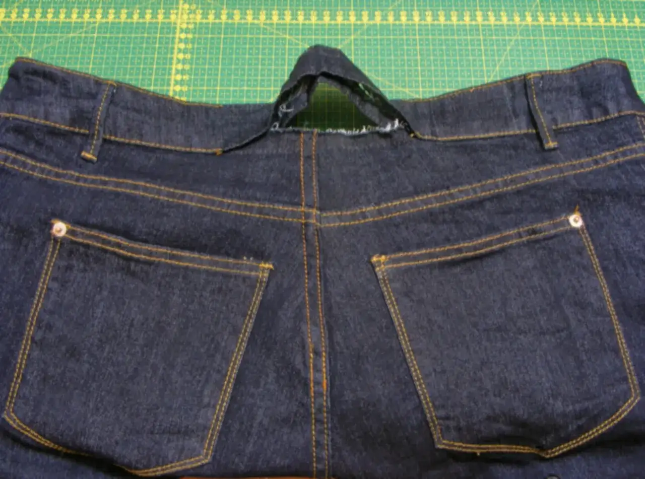 Tył dżinsów z widocznym miejscem na zwężanie spodni w pasie bez maszyny. Widać kieszenie i szwy.