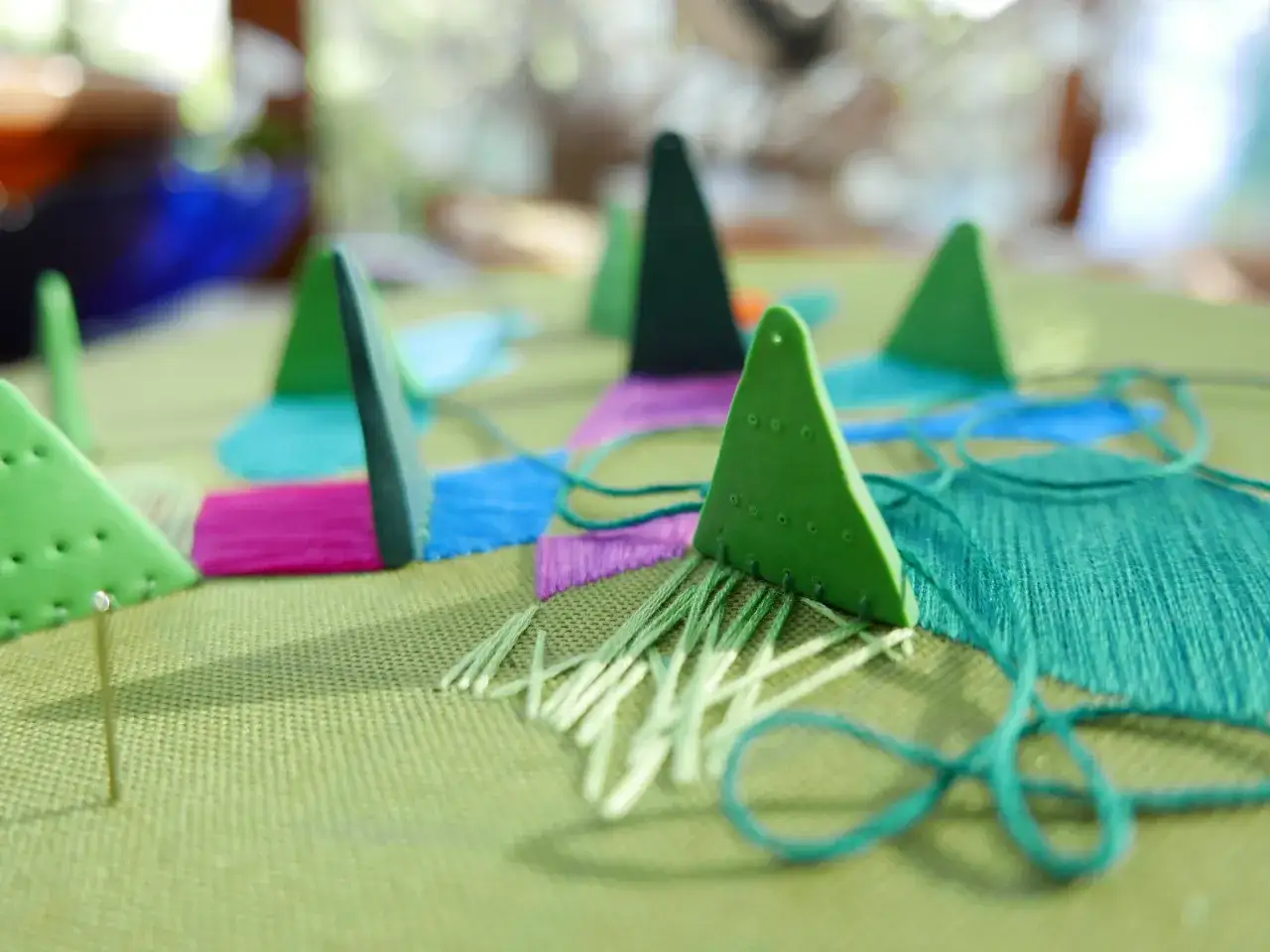 Kolorowe trójkąty pomagają w wyszywaniu na tamborku. Zielone nici tworzą wzór na tkaninie.