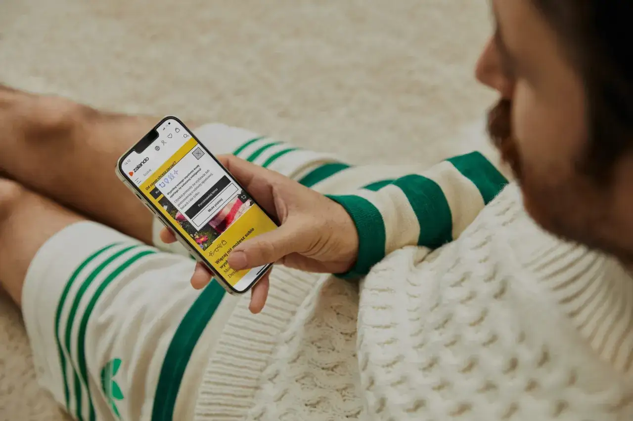 Mężczyzna sprawdza na telefonie, czy zalando jest legit, przeglądając aplikację z poradami stylistycznymi.