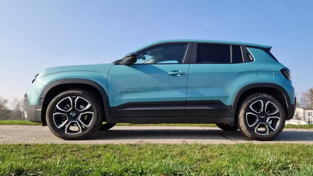 Turkusowy Jeep Avenger 4x4 z czarnymi felgami na tle nieba i trawy.