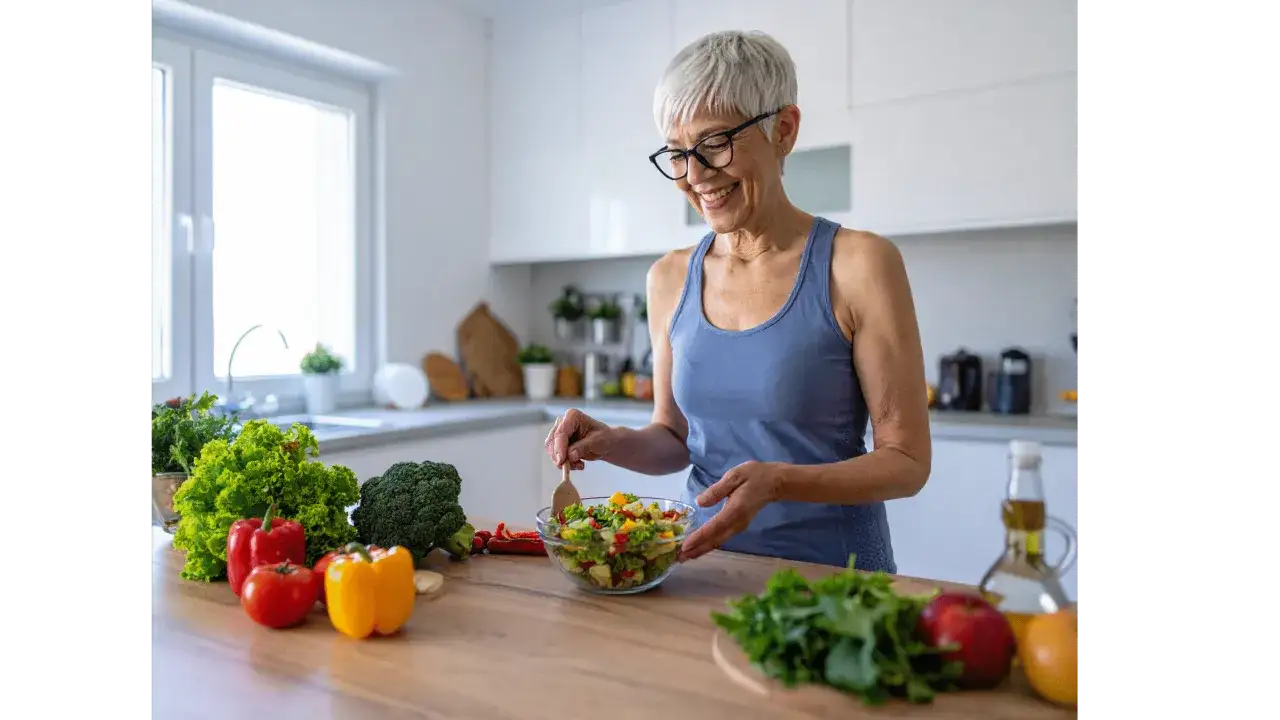 Uśmiechnięta starsza pani przygotowuje zdrową sałatkę. Pokazuje, co gotować starszej osobie: świeże warzywa i owoce.