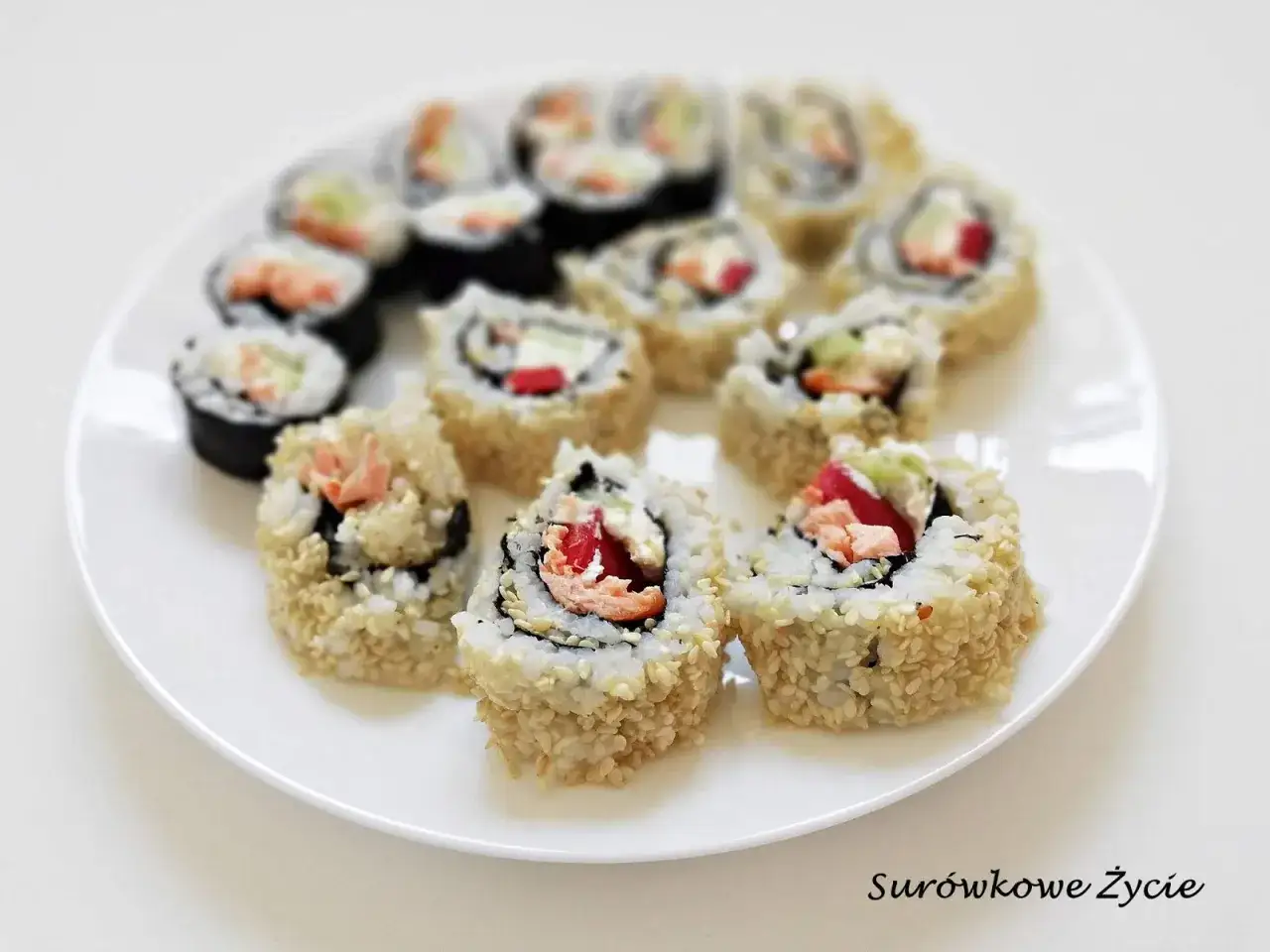 Talerz pełen sushi uramaki z łososiem, awokado i papryką, posypane sezamem. Pyszne i kolorowe rolki.