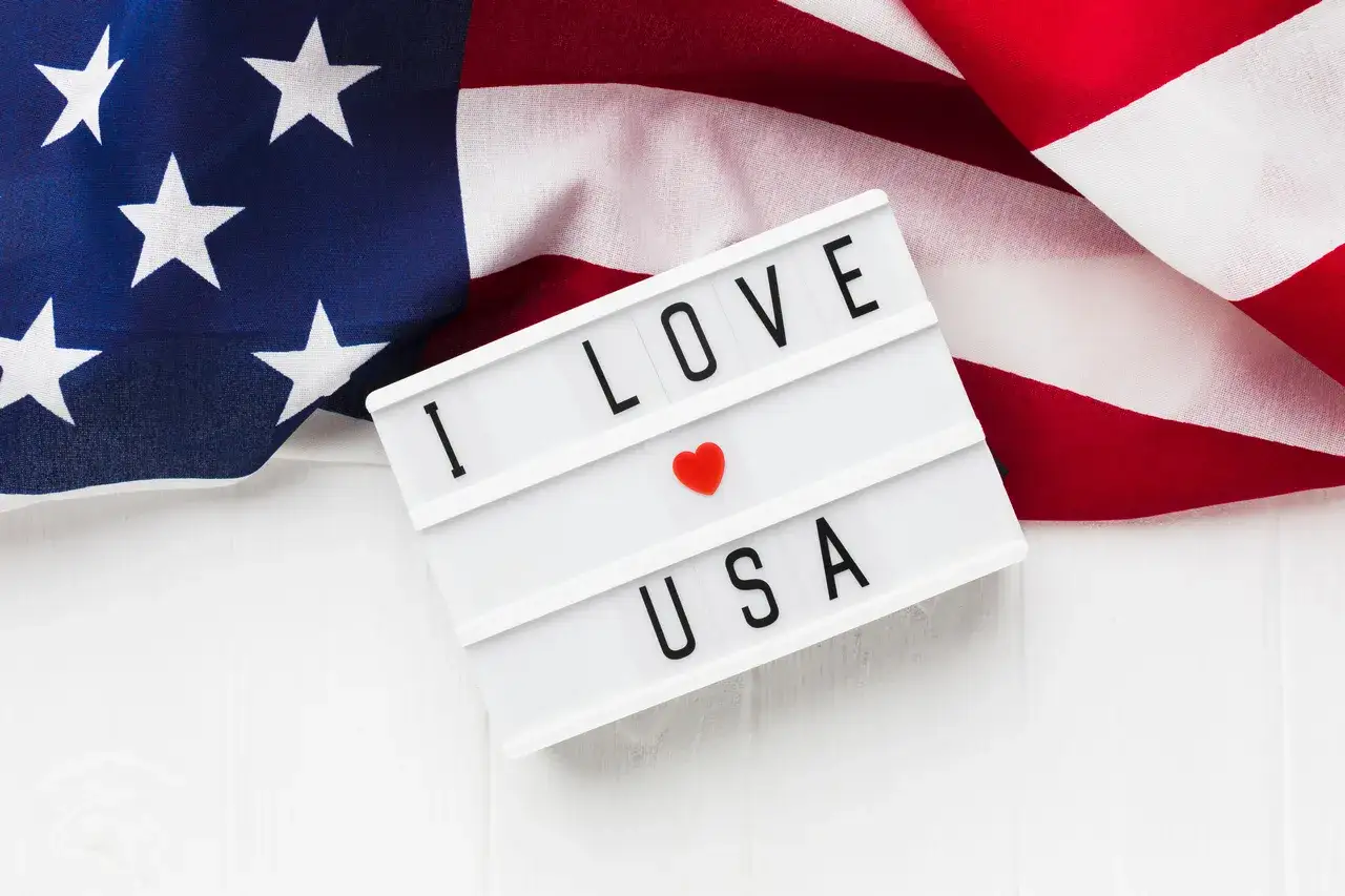 Amerykańska flaga i tablica z napisem "I LOVE USA". Zastanawiasz się, ile kosztuje bilet do USA w dwie strony?