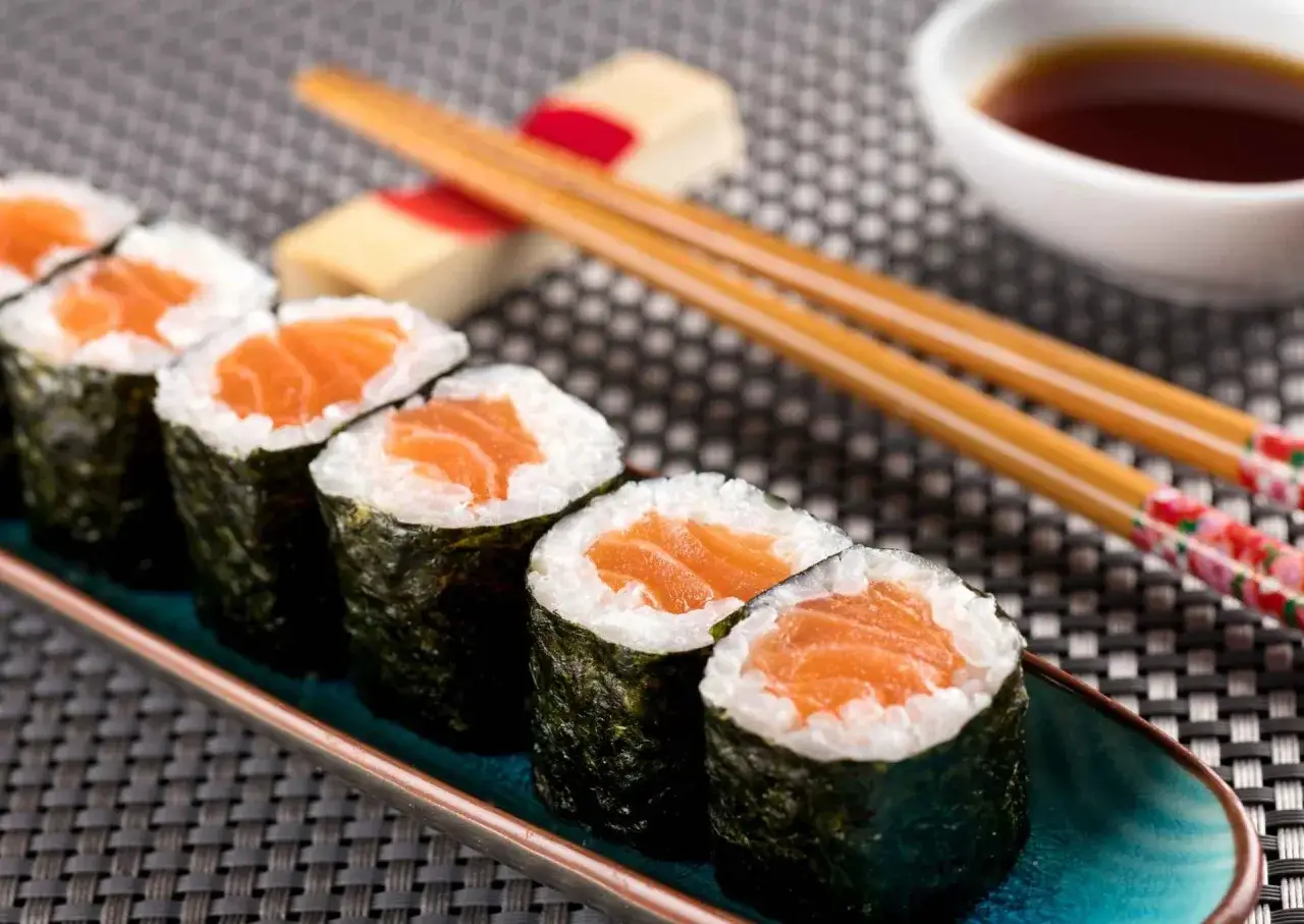 Rzędy hosomaki z łososiem, ryżem i wodorostami nori, pałeczki i sos sojowy.