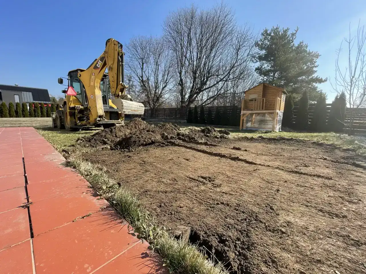 Koparka przygotowuje teren pod trawnik. Widać kopiec ziemi i wykopane rowy. Ile ziemi pod trawnik na m2?
