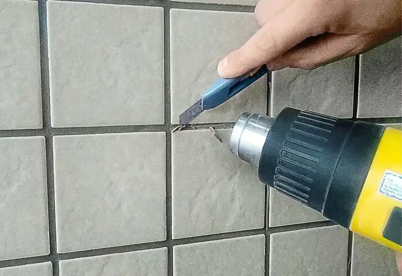 Usuwanie starej fugi epoksydowej na zewnątrz za pomocą opalarki i nożyka.