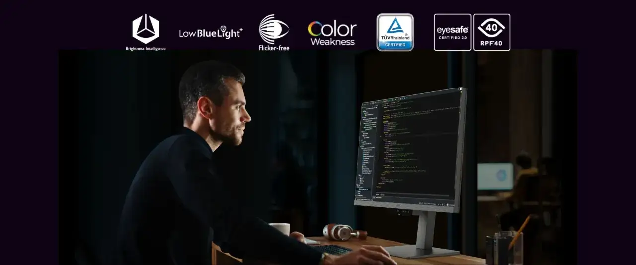 Mężczyzna pracuje przy monitorze z kodem, w tle inne osoby.