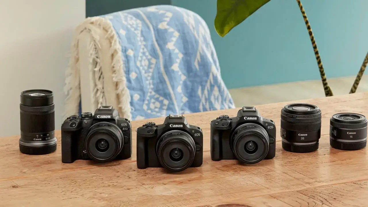 Trzy czarne aparaty Canon EOS z obiektywami i dodatkowe obiektywy na drewnianym stole.