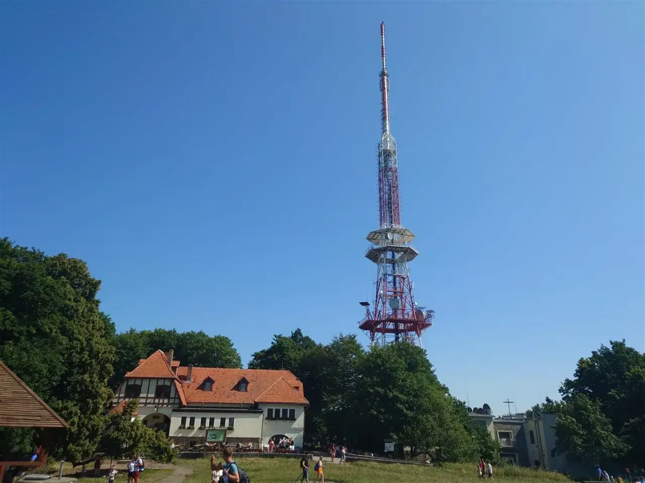 Wieża widokowa na górze Ślęża góruje nad budynkiem schroniska i zielonymi drzewami.