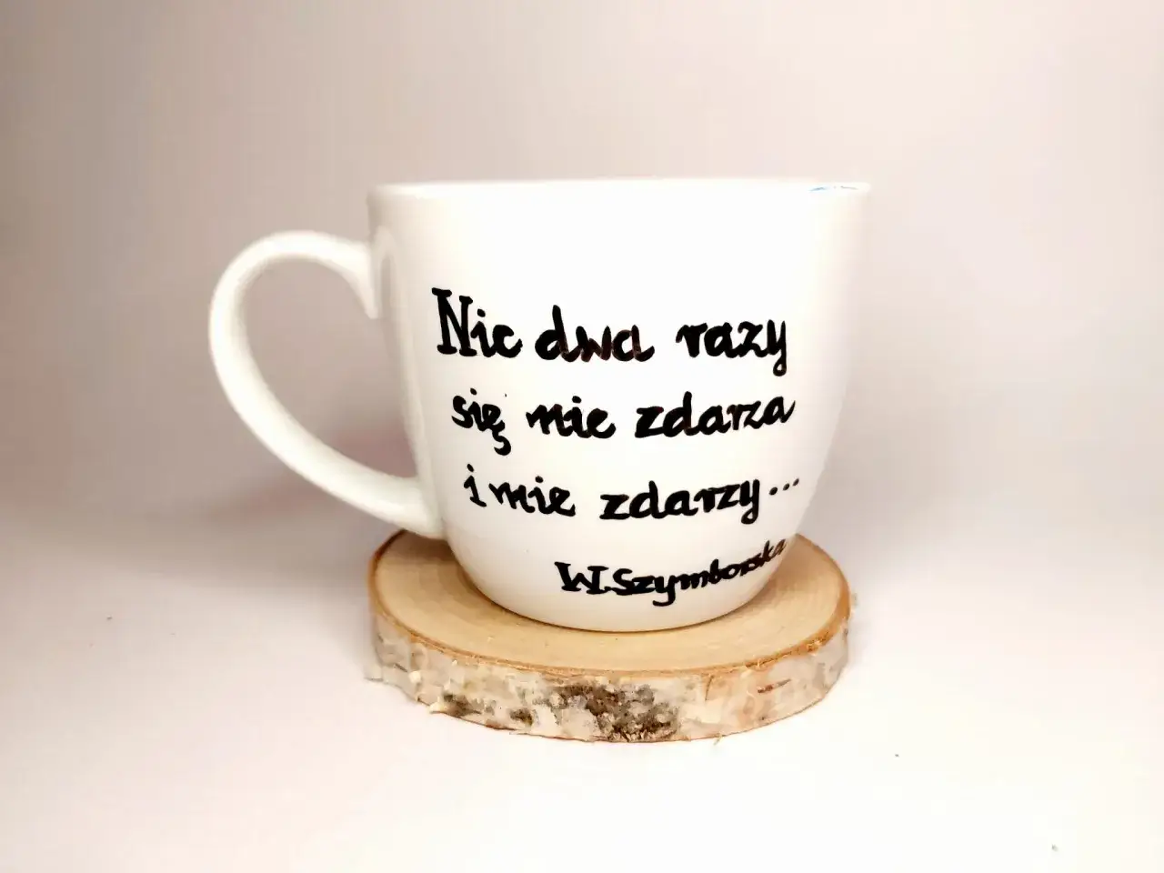 Biały kubek z cytatem Wisławy Szymborskiej: "Nic dwa razy się nie zdarza i nie zdarzy...". Wczoraj kiedy twoje imię ktoś wymówił przy mnie głośno wiersz.