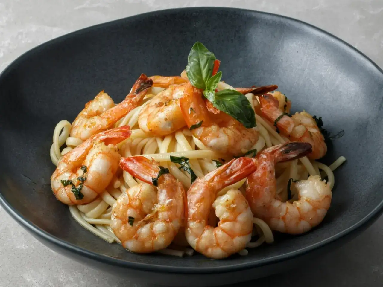 Pyszne dania z krewetkami na talerzu: makaron z soczystymi krewetkami i listkami bazylii.