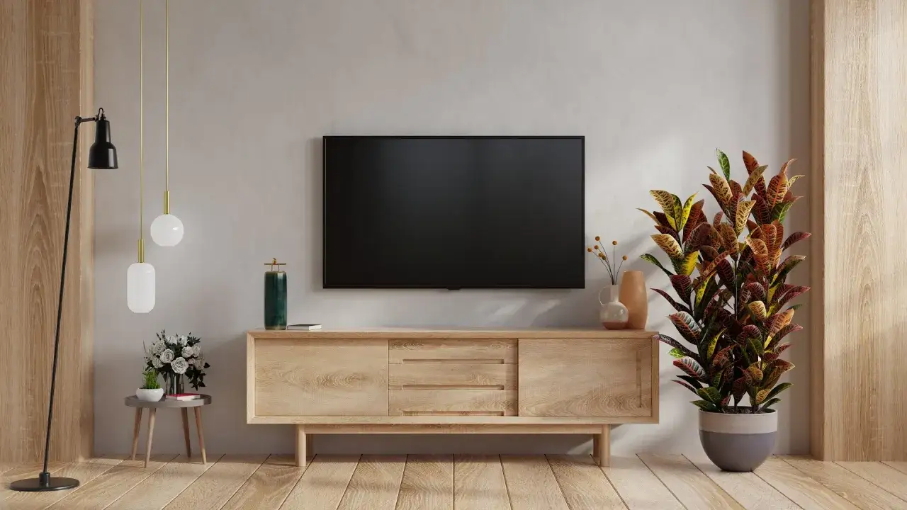 Nowoczesne aranżacje salonu z telewizorem na ścianie. Drewniana szafka RTV, lampa podłogowa i ozdobna roślina tworzą przytulną atmosferę.