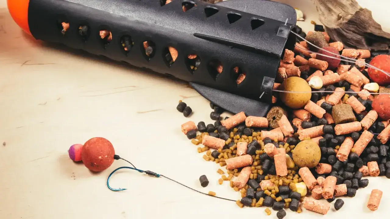 Czarny podajnik wędkarski z przynętą i haczykiem na drewnianym tle.