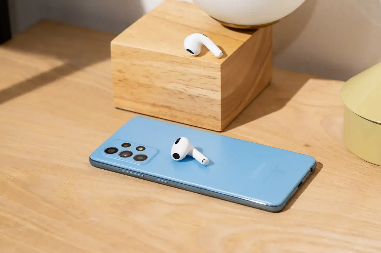AirPods liegen auf einem blauen Samsung-Smartphone und einem Holzblock.