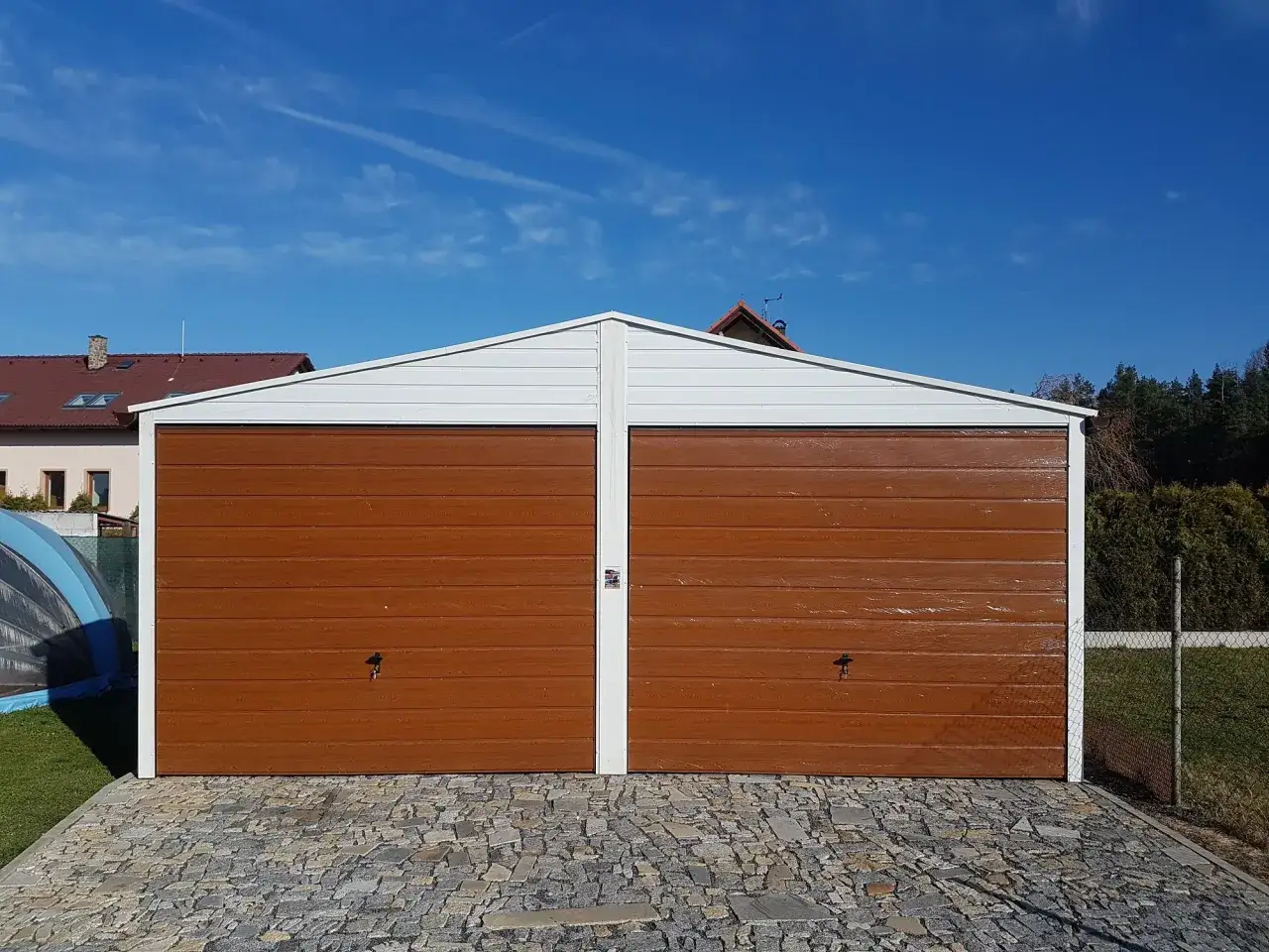 Dwustanowiskowy garaż blaszany z brązowymi drzwiami, stojący na kostce brukowej. Dowiedz się, jak zakotwić garaż blaszany do kostki brukowej.