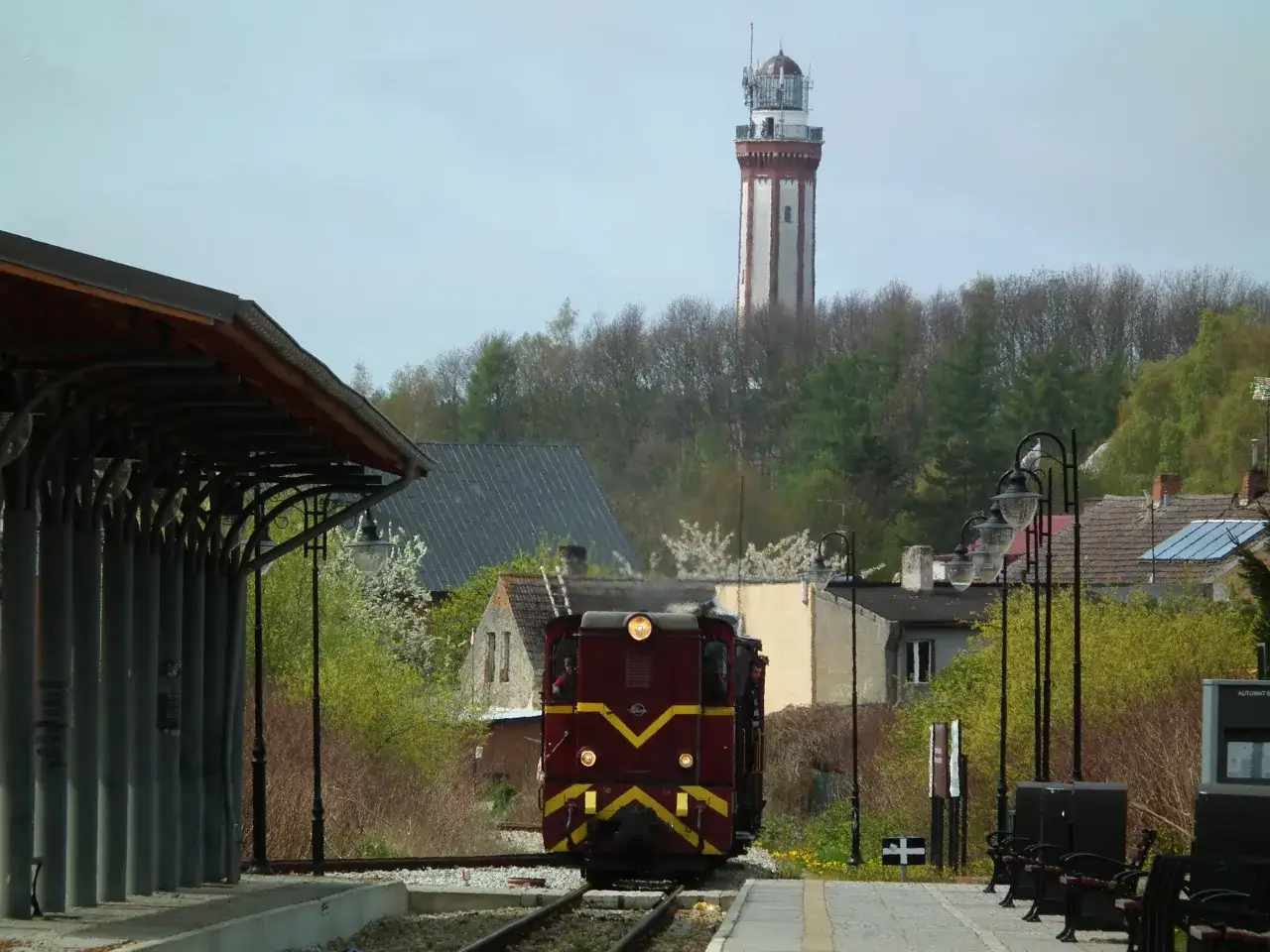Czerwony pociąg na tle latarni morskiej i drzew.