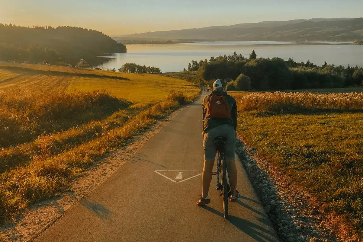 Rowerzysta na ścieżce rowerowej nad jeziorem w promieniach zachodzącego słońca.