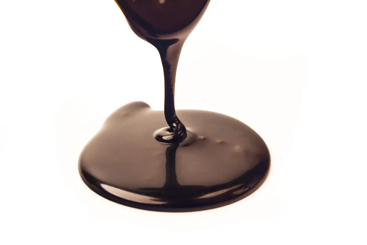 Gęsta, błyszcząca polewa czekoladowa spływająca na białe tło.