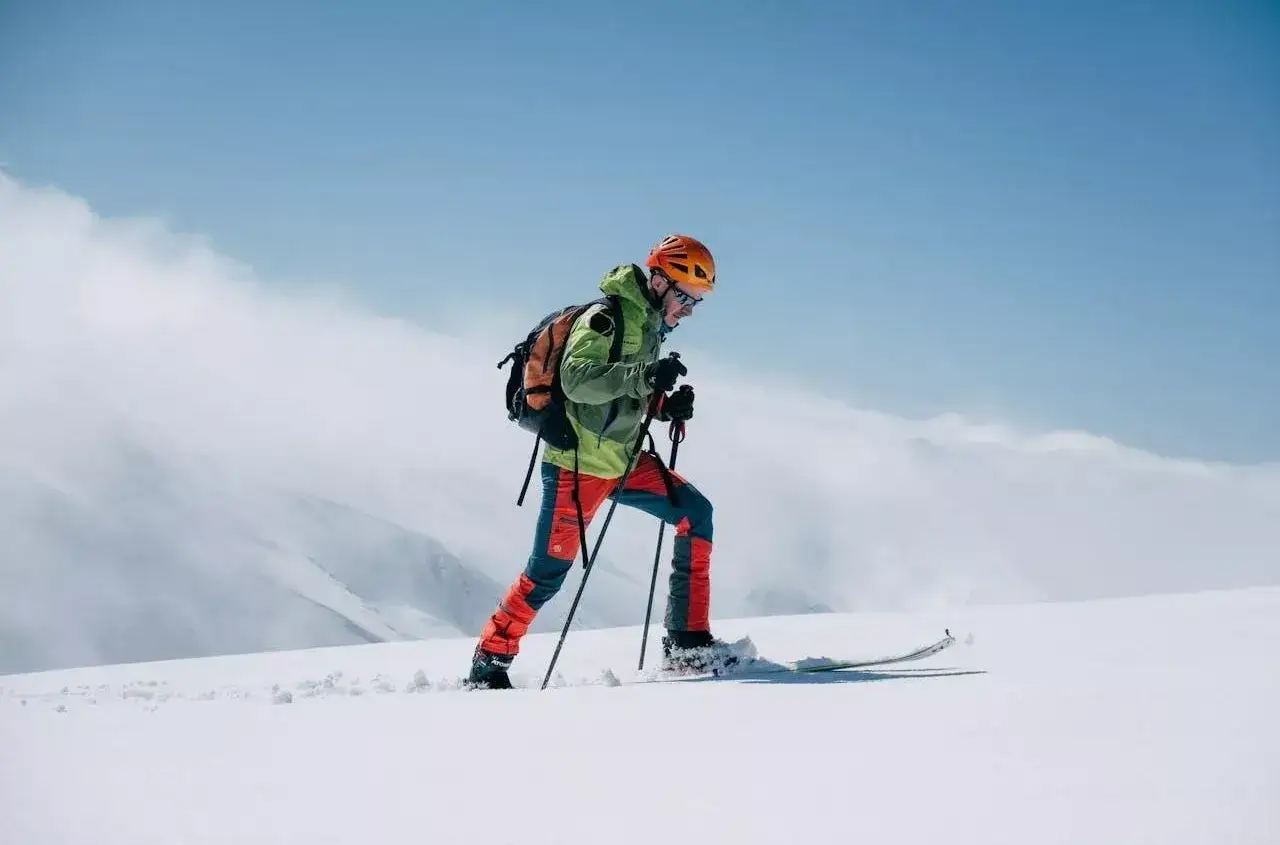 Narciarz w kasku i plecaku wspina się po śniegu. Twardość butów narciarskich zapewnia stabilność na stromym, zaśnieżonym zboczu.