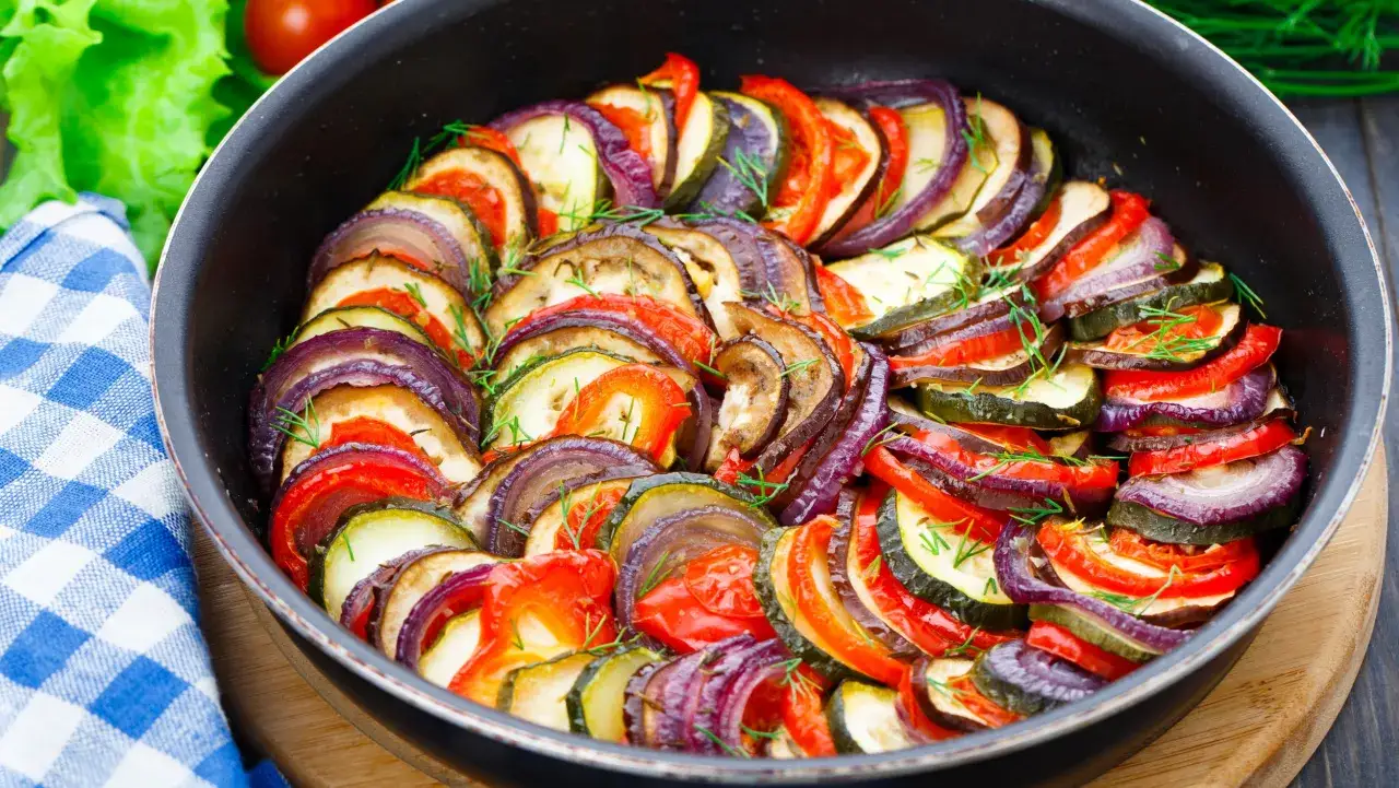 Ratatouille, charakterystyczne potrawy kuchni francuskiej, w naczyniu z warzywami: cukinią, bakłażanem, pomidorem i cebulą, przybrane ziołami.