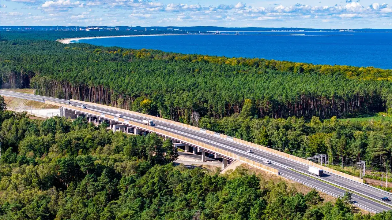 Droga S3 przebiega przez malowniczy las, wznosząc się nad drzewami. W oddali widać błękitne morze i wybrzeże.