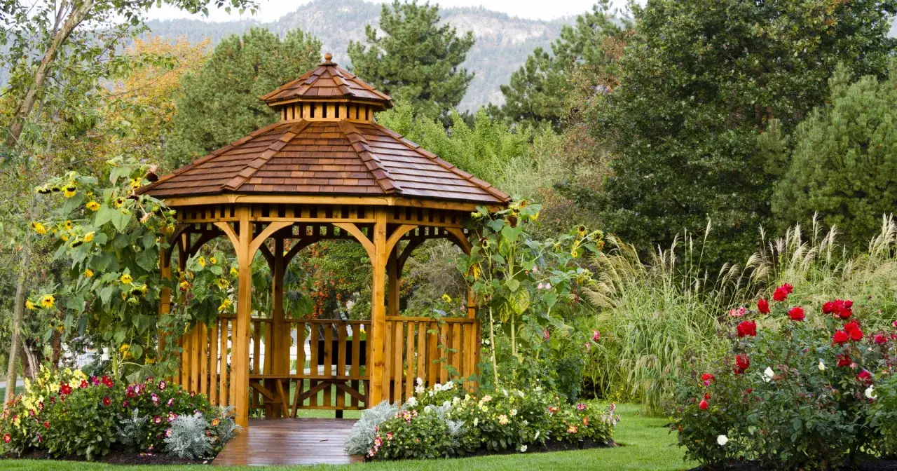 Drewniana altana w otoczeniu kwitnących słoneczników i róż. Idealne miejsce, by zastanowić się, czym pomalować altanę, by służyła latami.