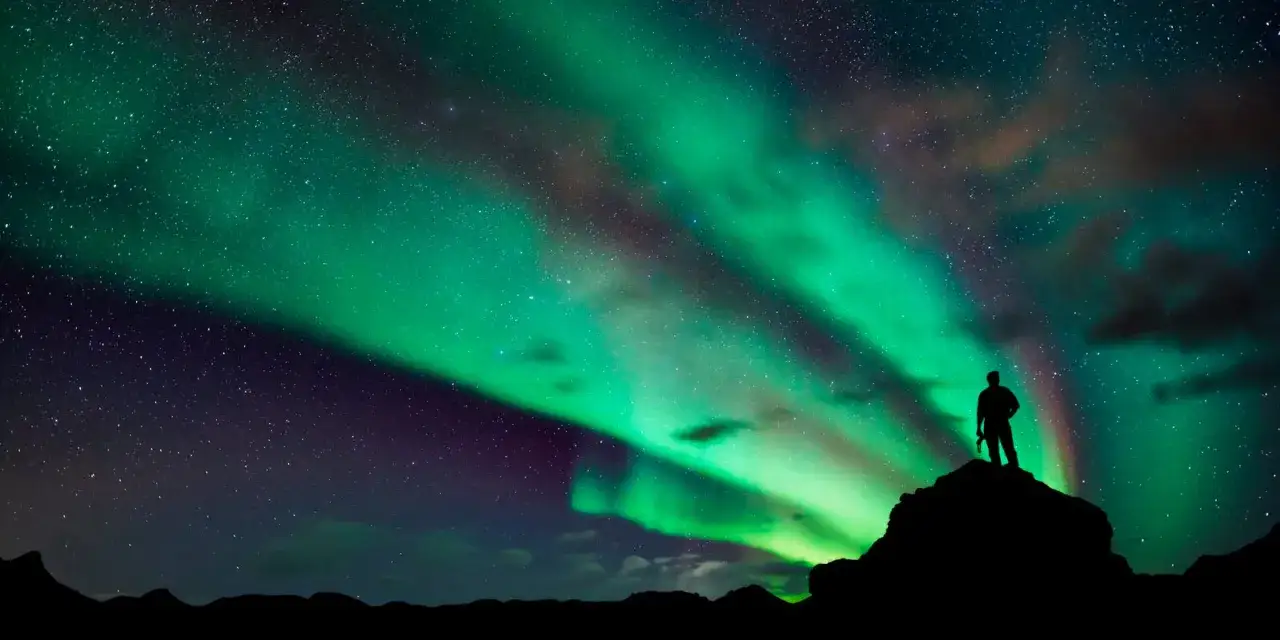 Sylwetka człowieka na skale podziwia zorzę polarną. Czy na Antarktydzie jest zorza polarna? Tak, to dowód!